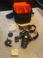 Overview of camera kit items including body, lens, case, manual, battery, charger, strap, cap and silver accessory