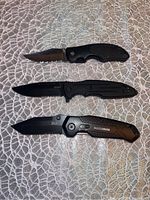 Three pocket utility knives laid flat showing closed handles and open blades; top and bottom knives have partially serrated blades, middle knife with a straight blade.