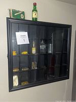 Front view of wooden wall-mounted display case with glass cover showing multiple compartments containing small collectible items.