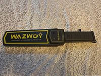 Top view of the Wazwoy hand-held metal detector showing full length on lace fabric background.
