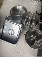 Photo showing two oval serving trays, two rectangular covered pans stacked inside a large stainless steel bin, and a smaller cylindrical bin