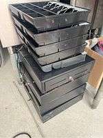 Stack of four black electronic cash registers each with a removable cash tray on top showing compartments and clips for organizing money, power cords visible