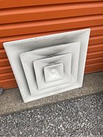 Front side of square white metal ceiling vent grate with stepped concentric design.