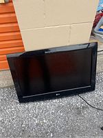 Front view of LG 32-inch flat screen TV with black frame resting on gravel against a wall.
