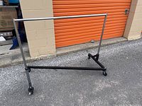 Front view of the metal coat rack showing the horizontal hanging bar and black base with wheels.