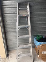Metal ladder standing in front of storage unit, showing steps and side rails