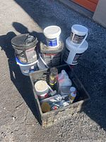 Photo showing multiple large buckets stacked including black and white buckets, with a black plastic crate containing various construction products.