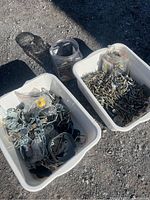 Two plastic bins with assorted metal and plastic hardware including brackets, clamps, rings, and chains alongside a jar of screws.