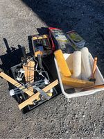 Overview of miscellaneous painting supplies showing paint rollers with covers, brushes, paint trays, roller frame, and packaged roller covers on ground.