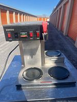 Front view of Newco commercial coffee maker showing control panel with switches, indicator lights, and hot water dispenser lever.