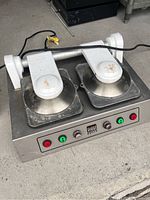 Front angle view of the Viva Grill double panini press showing the stainless steel base, two circular grill plates with white hinged lids, and front control panel with buttons and indicator lights.