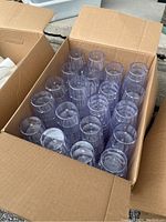 Open U-Haul cardboard box filled with multiple clear plastic drinking glasses placed upright, showing round rims and transparent bodies.