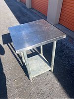 Angled front view of the stainless steel commercial table placed outside, showing the top surface and legs.