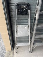 Front-facing view of the step ladder showing the two steps and black platform with circular holder against a wall.