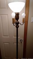Full view of antique floor lamp turned on showing large top tri light and three smaller bulbs on arms with candle-like holders.