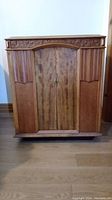 Front view of refinished wood antique radio cabinet with closed doors and carved floral and fluted detailing.