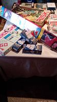Photo showing Monopoly, Risk, Battleship, and Blokus board games on table with domino sets and kite packaging visible