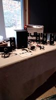 Photo of the Cyber Acoustics 5.1 surround sound speaker system components: one subwoofer, five satellite speakers, and visible cables on a table.