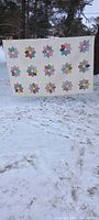 Front view of twin quilt displayed outdoors showing rows of colorful flower applique designs on white background.