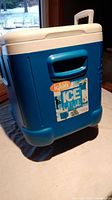 Blue and white Igloo cooler on a table showing front, side handle, and brand sticker.