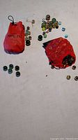 Photo of two red bags containing various marbles spread out on a white surface showing diversity in size and color