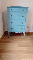 Front view of the light blue painted 4 drawer antique dresser with gold-tone handles and turned legs on casters.