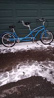 Full side view of blue tandem bike against garage door with light snow on ground