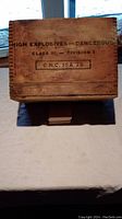 Top view of wooden munitions crate showing stenciled warning text: 'HIGH EXPLOSIVES -- DANGEROUS CLASS III -- DIVISION 1, C.R.C. 15A 75'