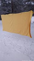 Yellow wool blanket hanging outdoors in snow, showing full side with yellow satin trim edges visible