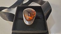Close-up photo of amber ring, showing smooth teardrop amber stone with visible seed inclusions, set in sterling silver.