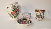 Four-piece lot with vase, lidded box, cup and small dish arranged on white background.