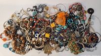 Overview of assorted costume jewellery including necklaces, bracelets, earrings, and rings in multiple colors and materials forming a large pile on white background.