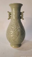 Front view of celadon vase showing detailed phoenix and dragon relief with ear handles.