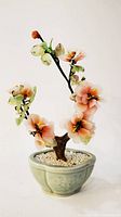 Glass jade flower tree with translucent pink, orange flowers and green leaves on dark branches in celadon ceramic pot with white gravel base.