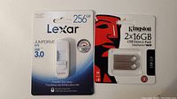 Front view of Lexar 256GB JumpDrive S75 USB 3.0 flash drive and Kingston 2-pack 16GB USB 2.0 flash drives in original sealed packaging.