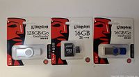 Front view of three unopened Kingston data storage devices: one 128GB USB flash drive, one 16GB microSD card, and one 16GB USB flash drive in original packaging.