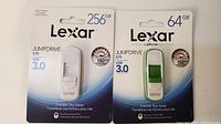 Front view of two Lexar JumpDrive S75 USB 3.0 flash drives in original packaging, showing storage capacities of 256GB (white) and 64GB (green).