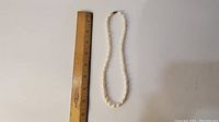 Full view of the pearl necklace next to a ruler to show length, approximately 18 inches.