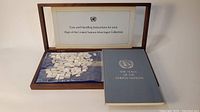 Wooden display case open showing blue felt interior with bag of silver mini ingots and instruction booklet