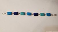 Full view of the bracelet laid flat showing seven rectangular blue stones alternating in turquoise and lapis colors linked with sterling silver, with lobster claw clasp.