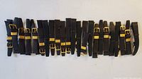 Top view of all 22 men's genuine leather watch bands arranged in a row, showing the textured black leather and gold buckle hardware.