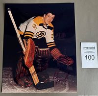 Color photograph of Bernie Parent in Boston Bruins uniform crouched in goalie position holding stick and wearing goalie gloves and pads.