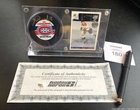Top view of the clear acrylic display stand containing the signed Montreal Canadiens puck and Henri Richard signed hockey card, with Certificate of Authenticity and pen placed next to them for scale.