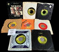 Eight 45 RPM records laid out showing original and generic sleeves with visible Apple Records and London Records logos, and a prominently visible Beatles Let It Be sleeve and label.