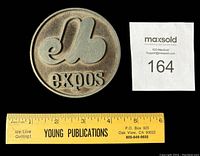 Front side of the round pewter coaster showing the raised Montreal Expos logo and name, next to a ruler indicating size of about 3.5 inches.