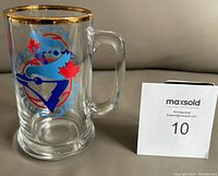 Clear glass beer mug with Toronto Blue Jays logo, handle, and gold rim shown from side angle.