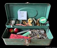 Top-down view of open green metal tackle box showing mixed vintage lures, hooks, weights, floats, spool of Salmo line, and other fishing items inside compartments.