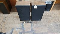 Front view of JVC speaker pair with black fabric covers standing on a wooden floor.