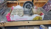 Mixed kitchen bakeware in a box including metal Bundt pan, muffin pan, clear glass baking dishes and loaf pans.