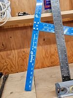 Blue Empire 48-inch drywall square leaning against the wall next to a silver metal square.